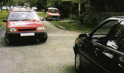 Slika uz pitanje: Vozač crvenog automobila namjerava skrenuti ulijevo u situaciji kao na slici. Vi kao vozač crnog automobila vozite ravno. Kako ćete postupiti?