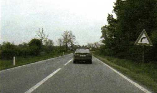Slika uz pitanje: Kako treba voziti zavojem u situaciji kao na slici?